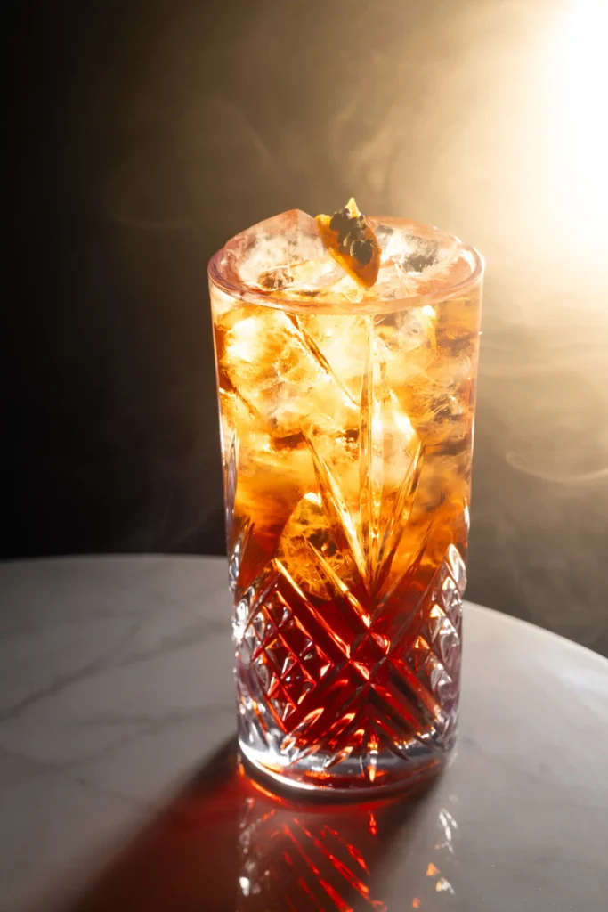 Cocktail ambré en contre-jour dans un verre ciselé, photo culinaire de bar – Cotta, Romans-sur-Isère