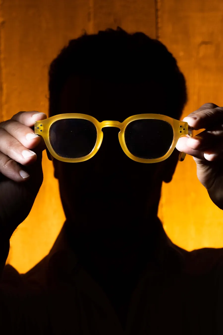 Lunettes jaunes tenues devant le visage sur fond orange, portrait créatif en studio
