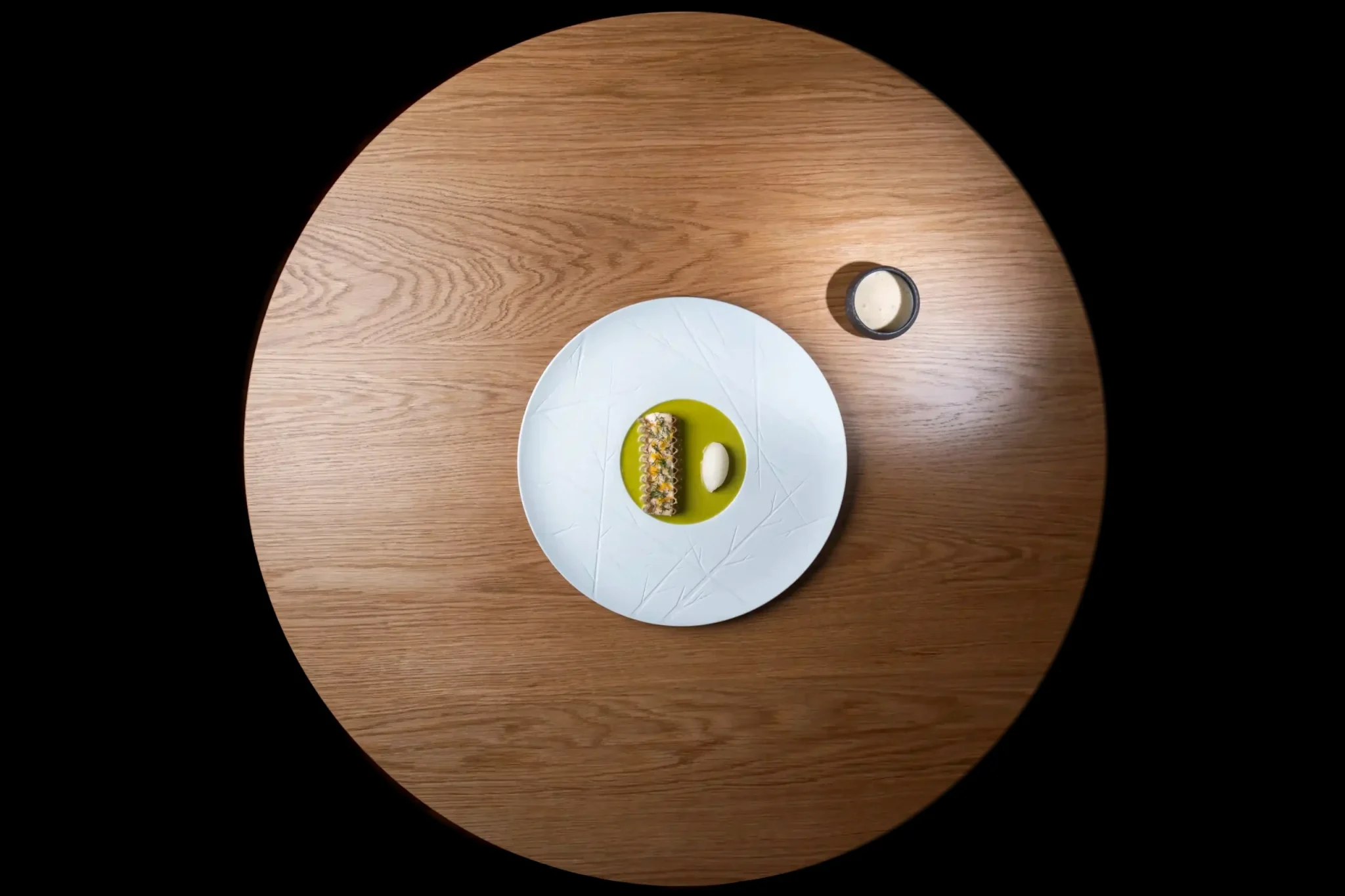 Assiette gastronomique sur table ronde en bois, vue du dessus, fond noir – photographe culinaire Studio 196